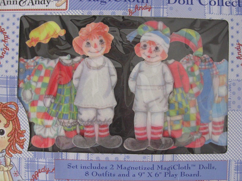 May include: A boxed set featuring two magnetized dolls and eight outfits. The dolls have red yarn hair, painted faces, and wear white outfits with red and white striped socks. The outfits include dresses and hats in various colors and patterns. The text on the box reads "Ann & Andy".