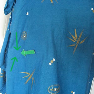 May include: Teal fabric featuring a pattern of gold bamboo-style designs and white and gold geometric shapes. The fabric is part of a garment, with a visible seam and a portion of a sleeve.