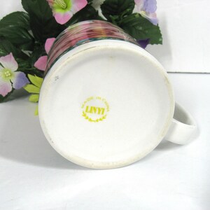 May include: White ceramic mug with a floral design and a yellow "LINYI" logo on the bottom. The logo is surrounded by a wreath and the words "MADE IN CHINA".
