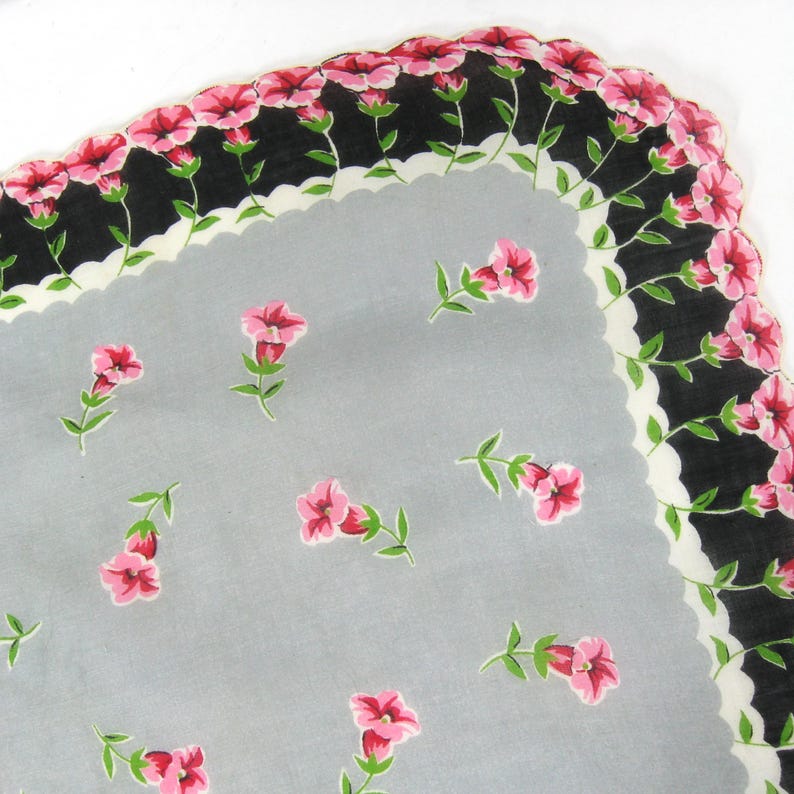 Pode incluir: Um len&ccedil;o vintage com fundo cinza e uma borda branca festonada. O len&ccedil;o &eacute; decorado com um padr&atilde;o repetido de flores cor-de-rosa com caules verdes.
