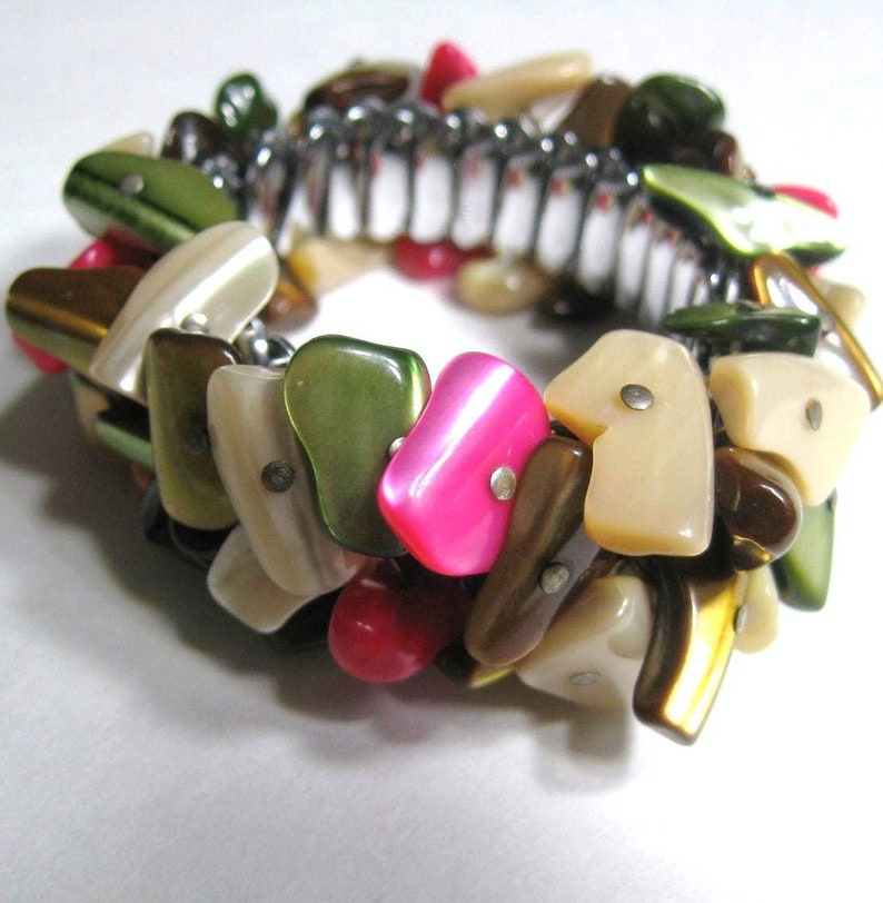 May include: A stretchy bracelet made of various colored and shaped shell pieces. The bracelet is made of brown, green, pink, and white shell pieces.