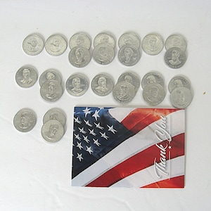 May include: A selection of silver commemorative coins with presidential portraits, alongside a card displaying the American flag. The card features the words "Thank You" in white script.
