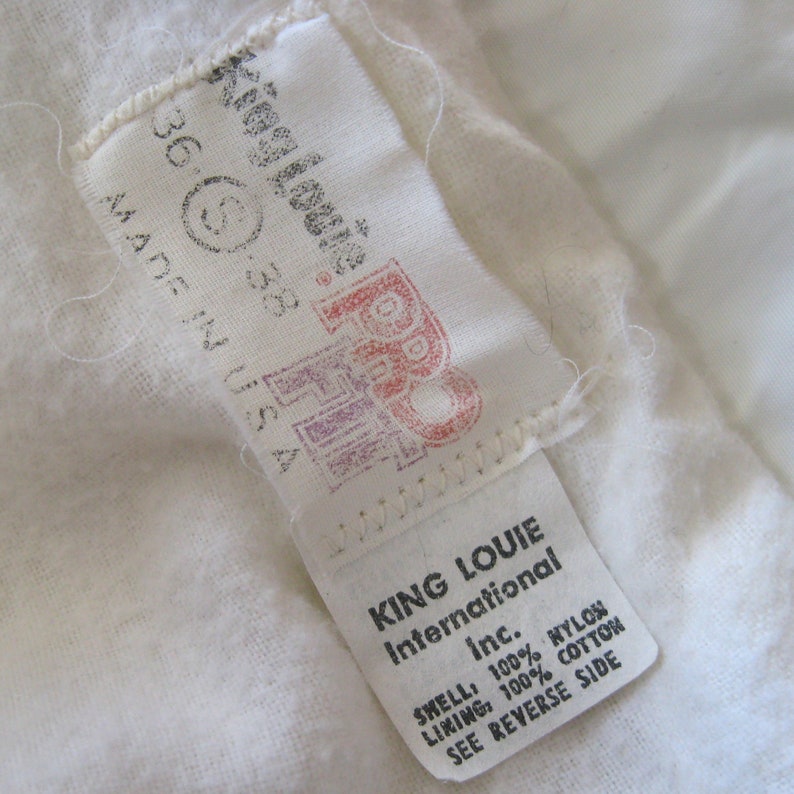 Pode incluir: Etiqueta branca com texto preto que diz "King Louie International Inc." e "Shell: 100% Nylon Lining: 100% Algod&atilde;o Veja o verso".