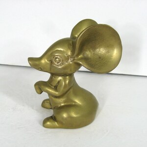 May include: A small, gold-colored brass mouse figurine with large ears. The mouse is sitting on its hind legs with its front paws raised.