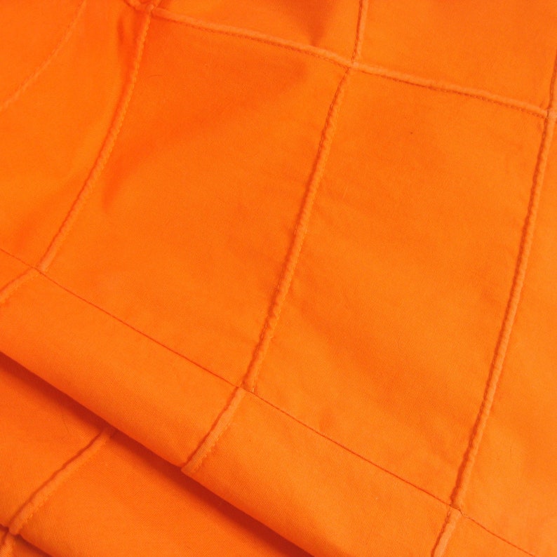 May include: Orange fabric with a quilted pattern. The fabric is folded in half, showing the stitching on the inside.