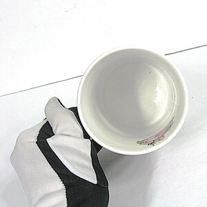 May include: White ceramic mug with a floral design. The mug is empty and the inside is visible.