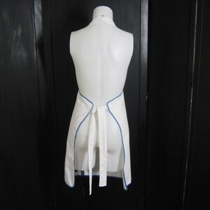 May include: White apron with a blue trim around the edges. The apron is tied at the back with a white ribbon.