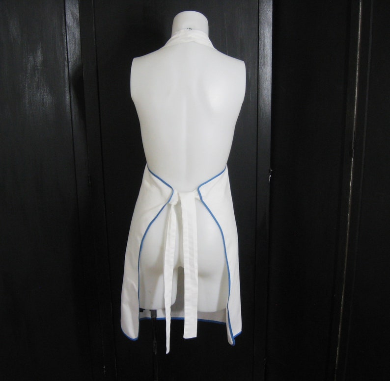 May include: White apron with a blue trim around the edges. The apron is tied at the back with a white ribbon.