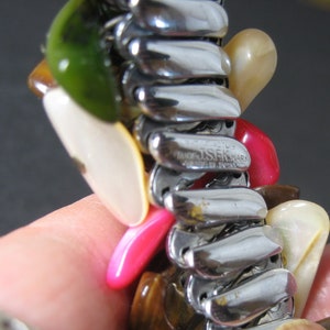 May include: A silver expandable bracelet with a variety of colorful stones, including green, white, pink, and brown. The bracelet is marked "J.S.K. MARK" and "PAT. PENDING".