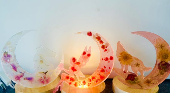 Real dried flowers pressed inside a glowing crescent moon — delicate, botanical, and clearly handcrafted rather than templated.