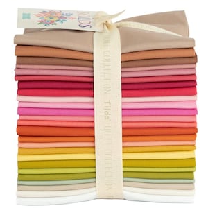 Puede incluir: Un conjunto de cuadrados de tela coloridos en varios tonos de rosa, rojo, naranja, amarillo y verde. Una cinta color crema envuelve la tela, y una etiqueta con diseños florales y la palabra "SOLIDS" está adjunta.