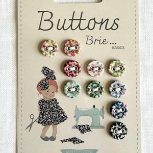 May include: A card of fabric-covered buttons in various floral patterns. The card features the text "Buttons Brie... BASICS" and an illustration of a girl with a sewing machine. The brand name "Tilda" is also visible.