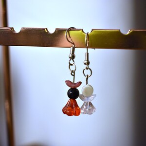 May include: A pair of dangle earrings with silver hooks and colorful beads. One earring has red, pink, and black beads, while the other has white and pink beads.