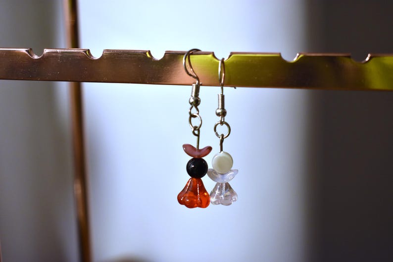 May include: A pair of dangle earrings with silver hooks and colorful beads. One earring has red, pink, and black beads, while the other has white and pink beads.