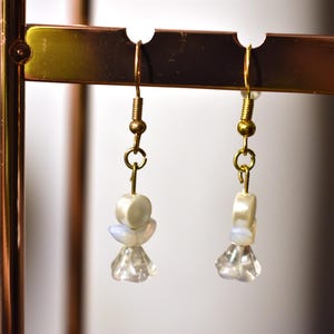 May include: A pair of gold dangle earrings with white and iridescent beads and clear crystal accents.