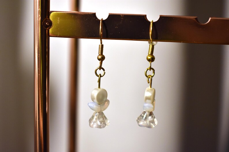 May include: A pair of gold dangle earrings with white and iridescent beads and clear crystal accents.