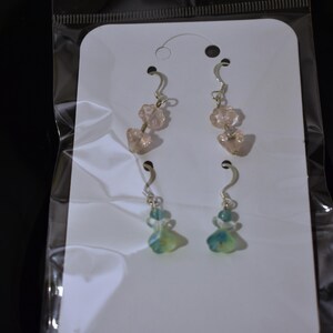 May include: A pair of earrings with pink and blue glass beads. The earrings are on a white card with a clear plastic backing.