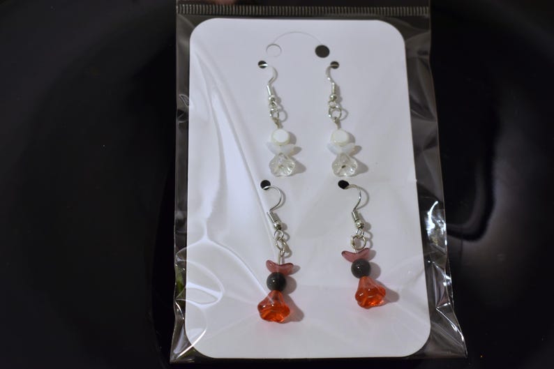 May include: A pair of earrings with white and clear beads and a pair of earrings with red and black beads.