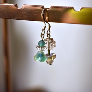 May include: A pair of dangle earrings with green and clear glass beads. The earrings are hanging from a gold hook.