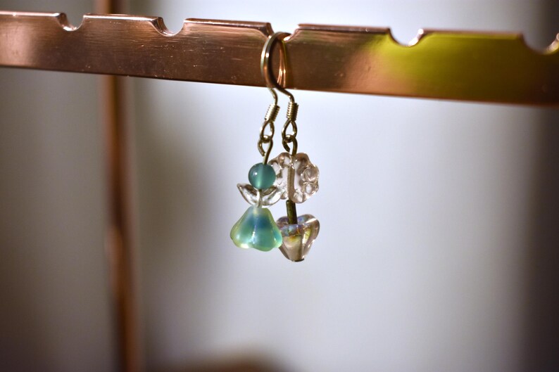 May include: A pair of dangle earrings with green and clear glass beads. The earrings are hanging from a gold hook.