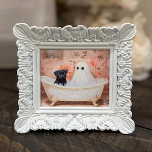May include: A framed artwork features a black pug dog and a ghost sharing a vintage bathtub. The artwork is set against a floral wallpaper background and framed in a white, ornate, distressed frame. The theme is Halloween.