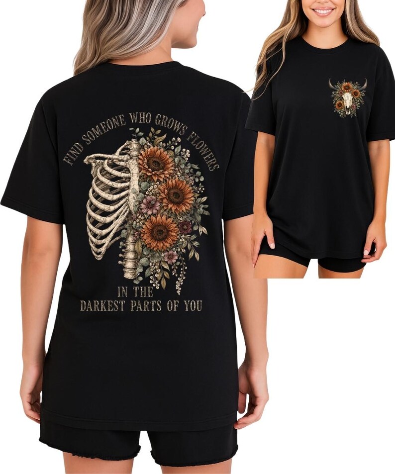 May include: Black t-shirt featuring a floral and anatomical design. The back of the shirt displays a rib cage with sunflowers and other flowers. Text on the back reads "FIND SOMEONE WHO GROWS FLOWERS IN THE DARKEST PARTS OF YOU". The front has a smaller design.