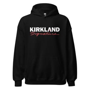 May include: Black hooded sweatshirt with the text "KIRKLAND Signature" in white and red script. The sweatshirt has a front pocket and a drawstring hood. The fabric appears to be a soft, comfortable material.