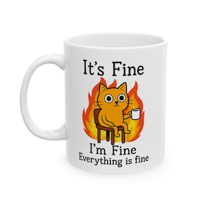 May include: White ceramic mug featuring a cartoon cat sitting in a chair, surrounded by flames, holding a coffee cup. The mug has the text "It's Fine, I'm Fine, Everything is fine" in black lettering.