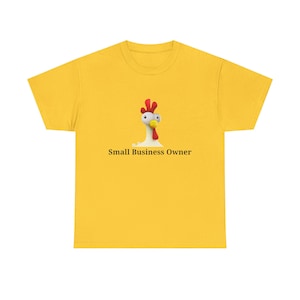 Puede incluir: Camiseta amarilla mostaza con un diseño de pollo de dibujos animados. El pollo tiene una cresta roja y un cuerpo blanco. El texto "Small Business Owner" está impreso debajo. La camiseta es de color sólido.