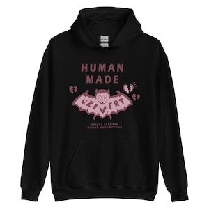 Pu&ograve; includere: Felpa con cappuccio nera con una grafica rosa di un pipistrello con il testo "HUMAN MADE" e "UZOVER" sul davanti. Il testo "BRIDGE BETWEEN HUMAN AND INHUMAN" &egrave; stampato sotto la grafica.