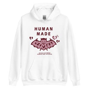 Pu&ograve; includere: Felpa con cappuccio bianca con una grafica di pipistrello rosso e il testo "HUMAN MADE" e "UZOVERT" con simboli di cuori spezzati. Il testo sotto la grafica dice "BRIDGE BETWEEN HUMAN AND INHUMAN".