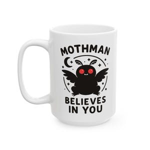 May include: White ceramic mug featuring a black cartoon Mothman design with red eyes, wings, and the text "Mothman Believes in You." The mug has a large handle and is suitable for hot or cold beverages.