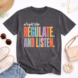 Puede incluir: Una camiseta de manga corta gris carbón con el texto blanco "alright stop" sobre el texto en letras de bloque de colores "REGULATE. AND LISTEN." en tonos naranja, verde azulado, amarillo y morado impreso en la parte delantera.