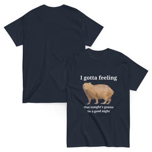 Pu&ograve; includere: Una t-shirt blu navy con un'illustrazione di capibara e il testo "I gotta feeling that tonight's gonna be a good night".