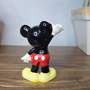 K&ouml;nnte beinhalten: Eine Keramikfigur von Mickey Mouse in klassischer Pose, mit schwarzem K&ouml;rper, roter Hose, wei&szlig;en Handschuhen und gelben Schuhen. Die Figur ist ein Sammlerst&uuml;ck, wahrscheinlich von Disney.