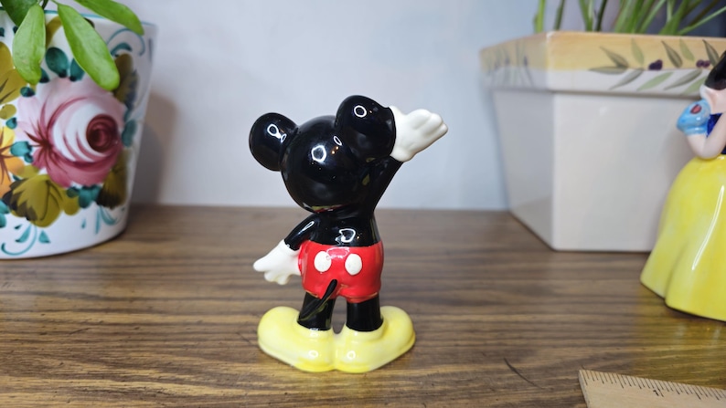 K&ouml;nnte beinhalten: Eine Keramikfigur von Mickey Mouse in klassischer Pose, mit schwarzem K&ouml;rper, roter Hose, wei&szlig;en Handschuhen und gelben Schuhen. Die Figur ist ein Sammlerst&uuml;ck, wahrscheinlich von Disney.