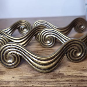 May include: A collection of antique brass-toned drawer pulls with a swirling, scroll-like design. The hardware is arranged on a wooden surface, showcasing their decorative and functional appeal. These pulls are ideal for adding a vintage touch to furniture.