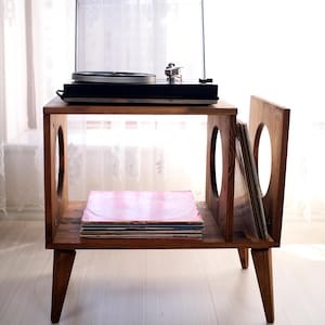Peut inclure: Un meuble pour platine vinyle en bois avec une platine noire. Le meuble a une étagère avec des disques vinyles et un compartiment latéral pour le stockage des disques. Le meuble est en bois foncé et a un design moderne du milieu du siècle. Hauteur: environ 76 cm.