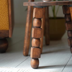 May include: A wooden side table with a round top and three legs. Each leg is made of stacked wooden beads and cubes.