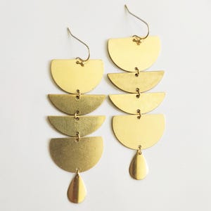 Könnte beinhalten: Goldfarbene Ohrringe mit einem kaskadierenden Design aus fünf abgestuften Halbkreisformen. Die Ohrringe haben einen tropfenförmigen Anhänger unten.