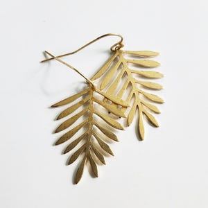 Op de afbeelding: Gouden bladvormige oorhangers. De oorbellen zijn gemaakt van metaal en hebben een delicaat, ingewikkeld ontwerp.