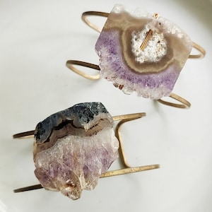 May include: Two gold metal bracelets with amethyst crystal accents. The crystals are a mix of purple, white, and brown.