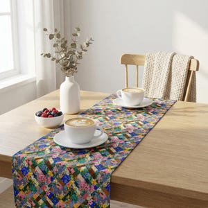 A colorful patchwork floral table runner styled on a light oak wood dining table. The bright morning setup features two large white ceramic mugs with latte coffee foam art, a small white bowl of fresh mixed berries, and dried eucalyptus branches in a modern white ceramic vase by a sunlit window.
