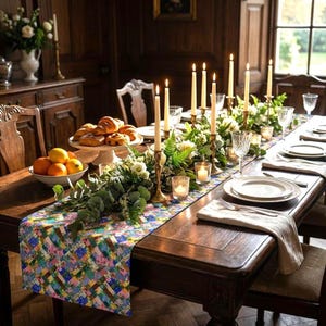 A vibrant patchwork floral table runner styled down a long, formal dark wood banquet table. The elaborate table setting features tall gold taper candlesticks, glowing votive candles, a lush eucalyptus and white flower garland, crystal glassware, a bowl of citrus fruits, and a platter of fresh croissants.