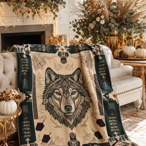 Peut inclure: Un plaid doux présentant une illustration centrale d'une tête de loup avec un travail de lignes géométriques complexe. Le motif comprend un fond crème avec des bordures bleu sarcelle foncé ornées de motifs de flèches et de losanges.