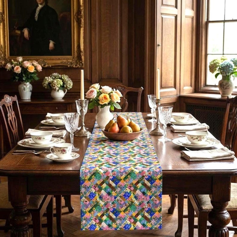 A vibrant patchwork floral table runner styled down a formal dark wood dining table. The classic interior features ornate wood paneling, fine china tableware, crystal goblets, silver candlesticks, and a center wooden bowl filled with fresh pears. Elegant roses and oil paintings decorate the background.