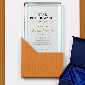 May include: A rectangular glass award plaque featuring the text STAR PERFORMANCE AWARD, PRESENTED TO Rohan Mehta, and a date of 25 May 2024. The plaque is partially encased in a light brown wooden holder and sits on a white card with printed text.