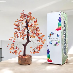 May include: A red carnelian crystal tree with a brown wooden base. The tree is in a white box with the text "The Crystal Cure" and "Cure Your Life With Crystals".