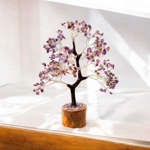 Peut inclure: Un arbre en cristal d'améthyste violet avec une base en bois. L'arbre est fait de fil de fer et a de nombreux petits cristaux qui y sont attachés.