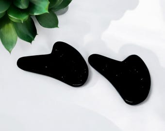 Peut inclure: Deux outils de gua sha en jade noir, en forme de croissant de lune, sur un fond blanc.